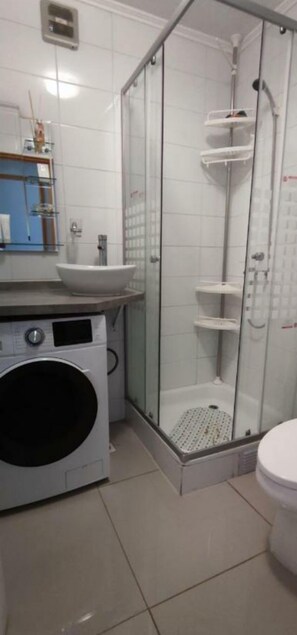 Un baño pequeño con ducha de mampara de vidrio, lavadora e inodoro.