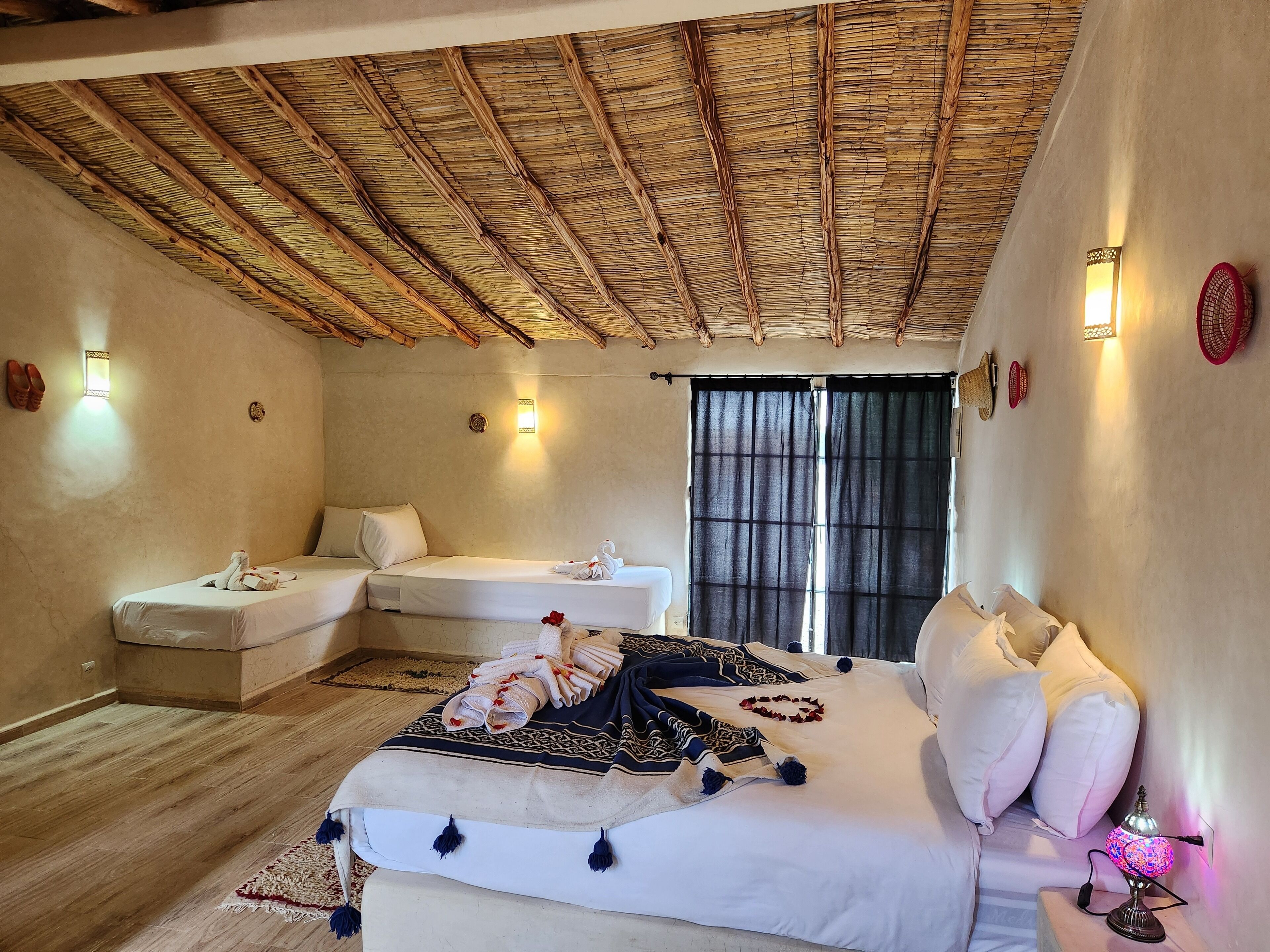 Une pièce comprenant un lit, un canapé, une fenêtre avec des rideaux et un plafond avec des poutres en bois.