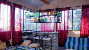 Une salle dotée d’un bar en pierre, de nombreux espaces pour s’asseoir et de grandes fenêtres ornées de rideaux rouges.