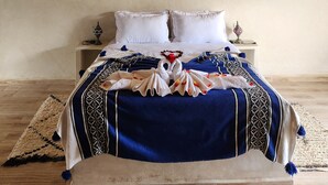 Une chambre à coucher avec un plafond haut recouvert de chaume, un lit avec des oreillers blancs et une couvre-lit à motifs bleus et blancs.