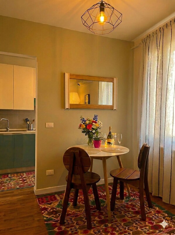 A dining area with a round table, two chairs, a vase of flowers, a bottle, and a glass.