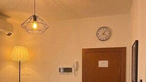 Ein Zimmer mit einem türkisblauen Sofa, einer Holztür, einer Wanduhr, einer Lampe und einem gemusterten Teppich.