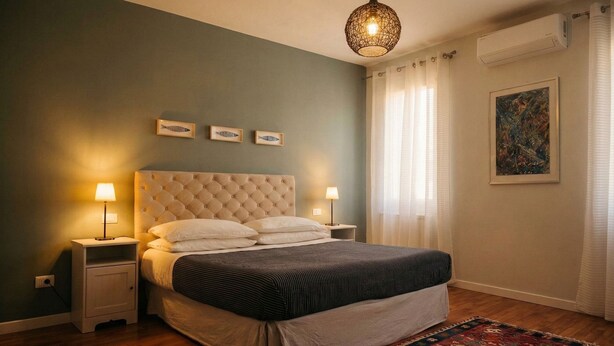 Ein Schlafzimmer mit einem geblümten Kopfteil, einem Bett mit gestreifter Bettwäsche, Nachttischlampen, einem gemusterten Teppich und einem Gemälde an der Wand.