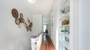 A hallway with a wooden floor, white walls, and a white bench with a purple cushion. - Hall Street Inn, Relaxing | Historic | Fresh (Savannah)