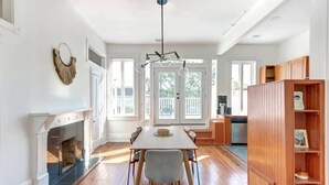 A spacious dining area with a fireplace, a large dining table, and a kitchen in the background. - Hall Street Inn, Relaxing | Historic | Fresh (Savannah)