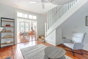 Ein modernes Wohnzimmer mit Holzdielenboden, einer Treppe, einem grauen Sessel und einem Bücherregal.