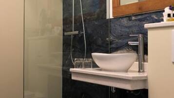Un baño moderno con ducha envuelta en vidrio, un lavamanos blanco y un espejo encima.