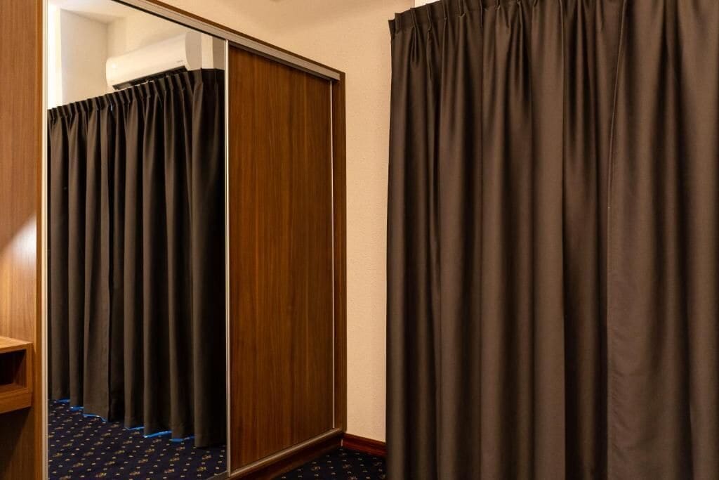 A hotel room with a wooden wardrobe, a mirror, and a dark curtain.