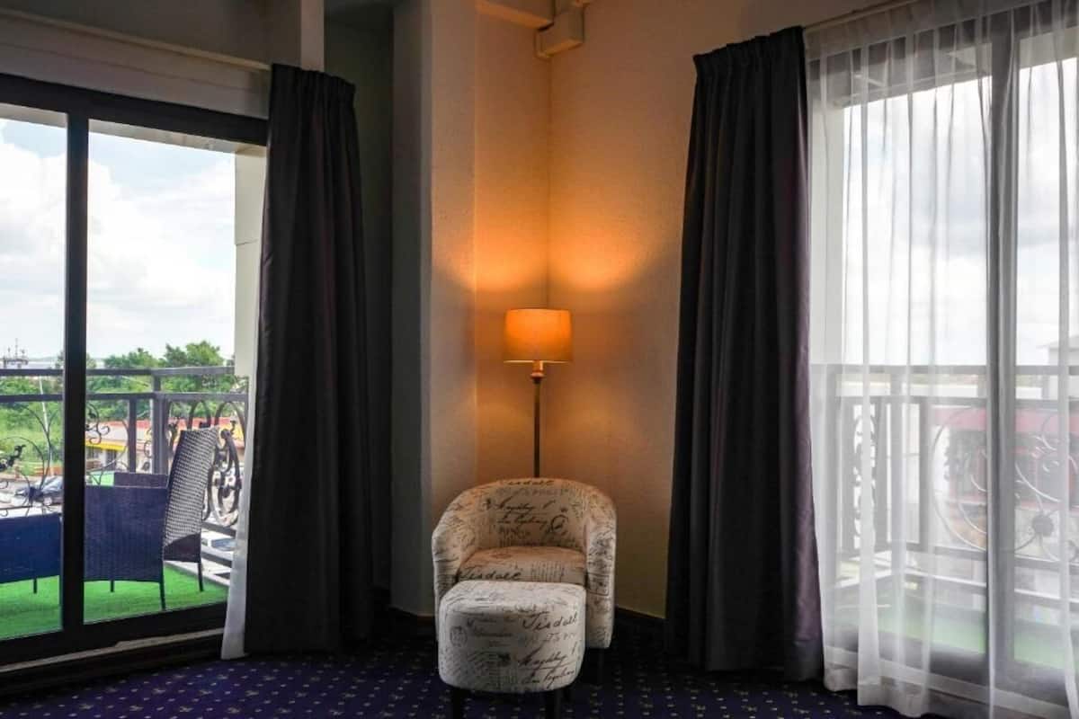 Une chambre d’hôtel dotée d’une grande fenêtre, d’un fauteuil, d’un lampadaire et d’un balcon offrant une vue sur l’extérieur.