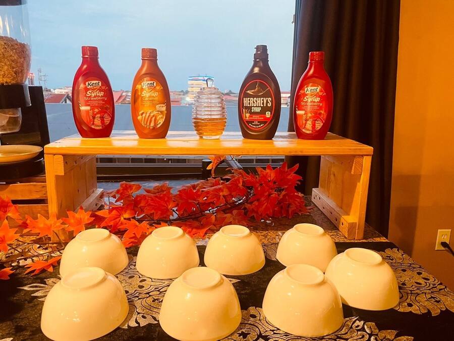A table with five bottles of syrup and six white ceramic cups.