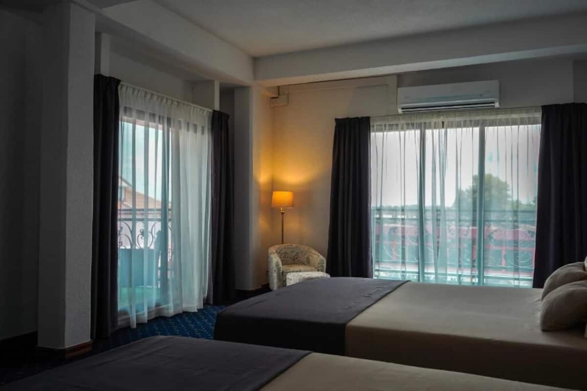 Une chambre d’hôtel avec deux lits, une chaise, une lampe et une vue sur la ville grâce à de grandes fenêtres.