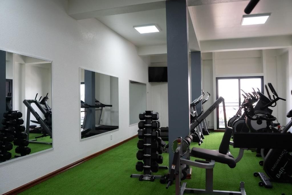 A gym with exercise equipment, mirrors, and green flooring.