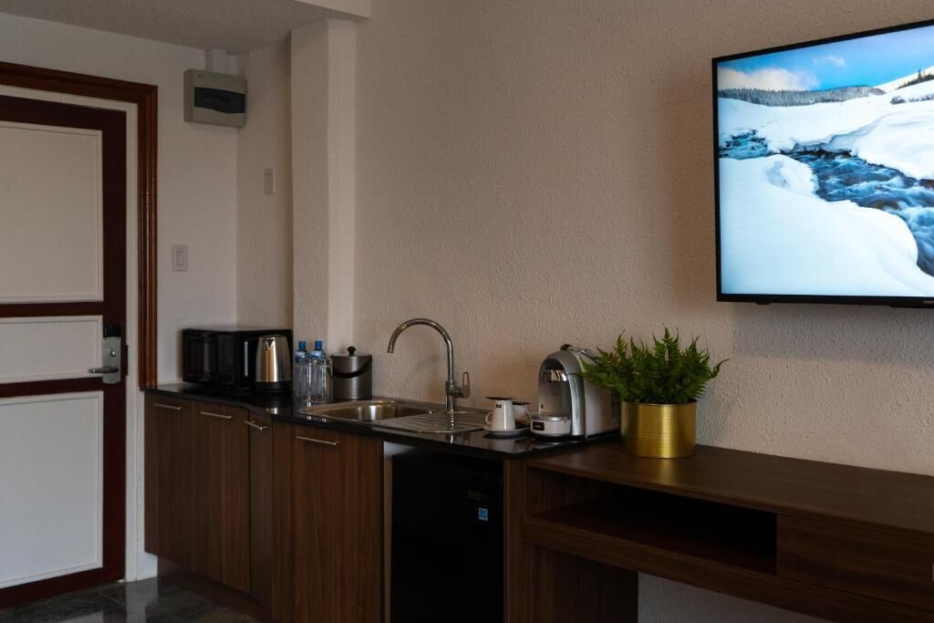 Eine kompakte Küche mit integriertem Geschirrspüler, Spüle und flach an der Wand montiertem Fernseher.