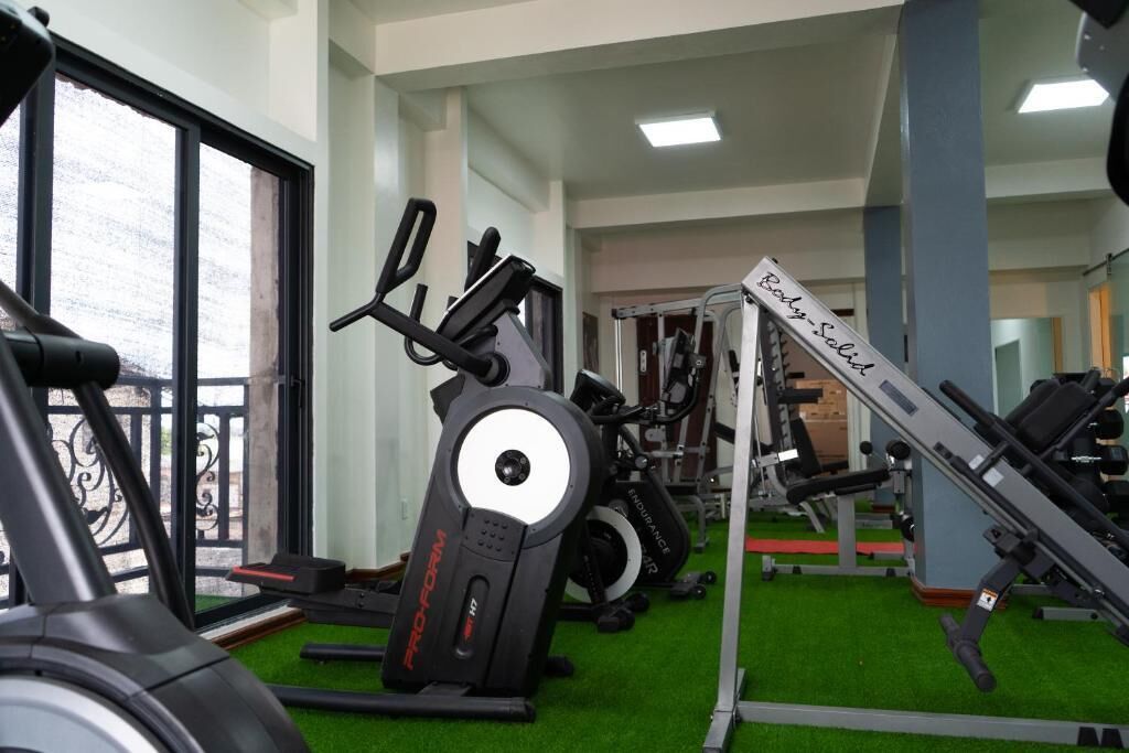 Uma academia com equipamentos de cardio, aparelhos de musculação e piso verde.
