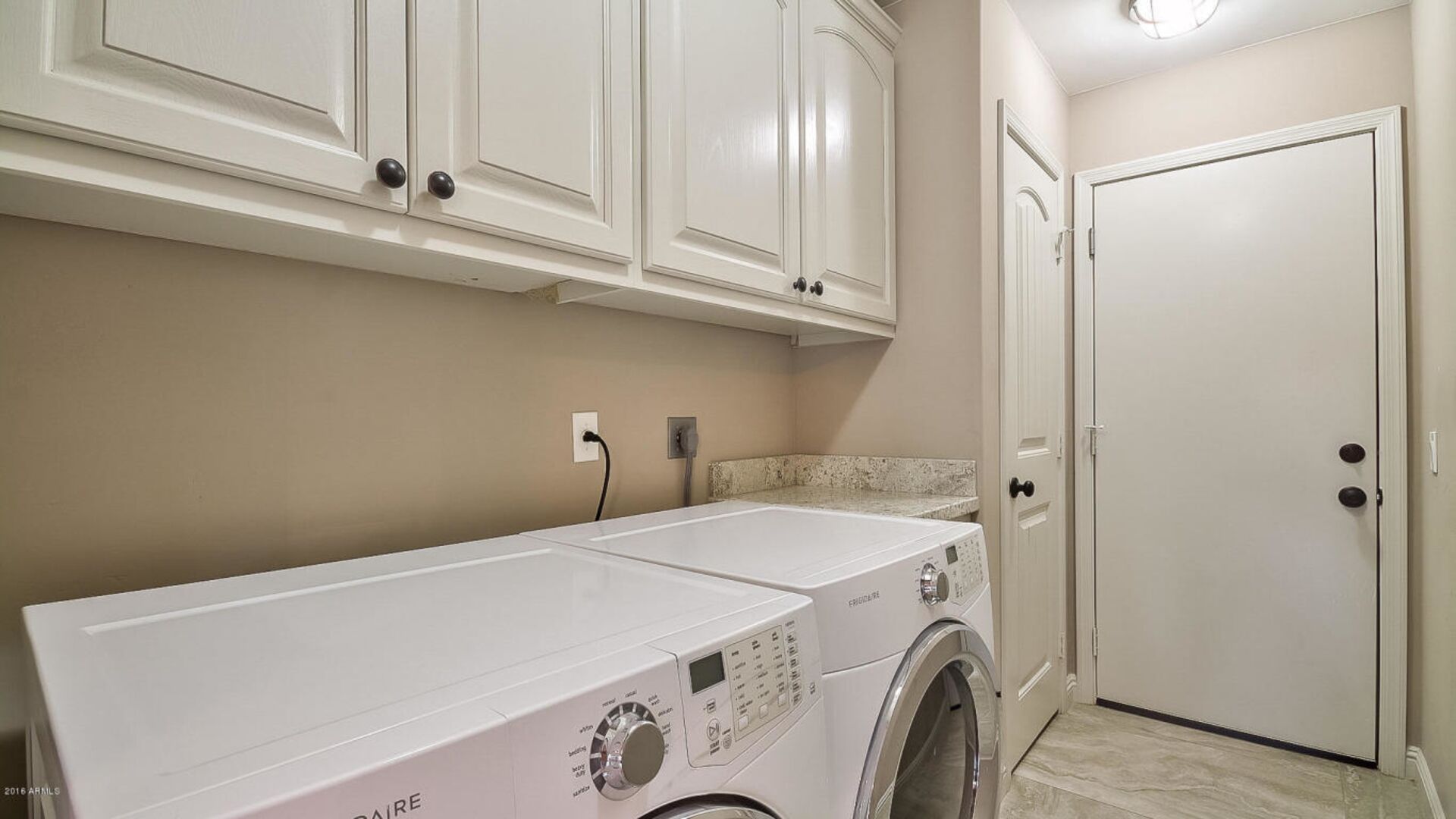 Une buanderie équipée d’un lave-linge à chargement frontal, avec des placards au-dessus et une porte sur le côté droit.