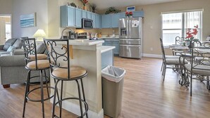 Una cocina moderna con armarios azules, un refrigerador de acero inoxidable y un comedor con sillas de metal.