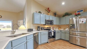 Una cocina moderna con armarios azul claro, electrodomésticos de acero inoxidable y un ventanal con vistas al exterior.
