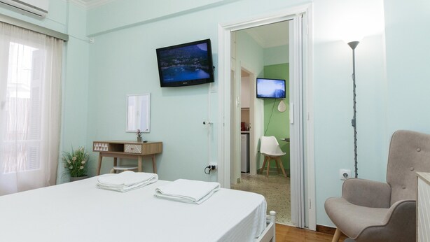 Ein Hotelzimmer mit einem Bett, einem Schreibtisch mit Lampe, einem Sessel und zwei Fernsehern an der Wand.