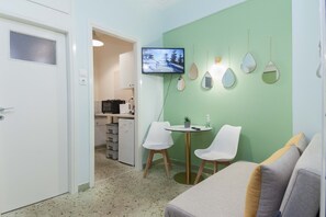 Espaço compacto com cozinha compacta, televisão na parede e área de estar com duas cadeiras e uma mesa pequena.
