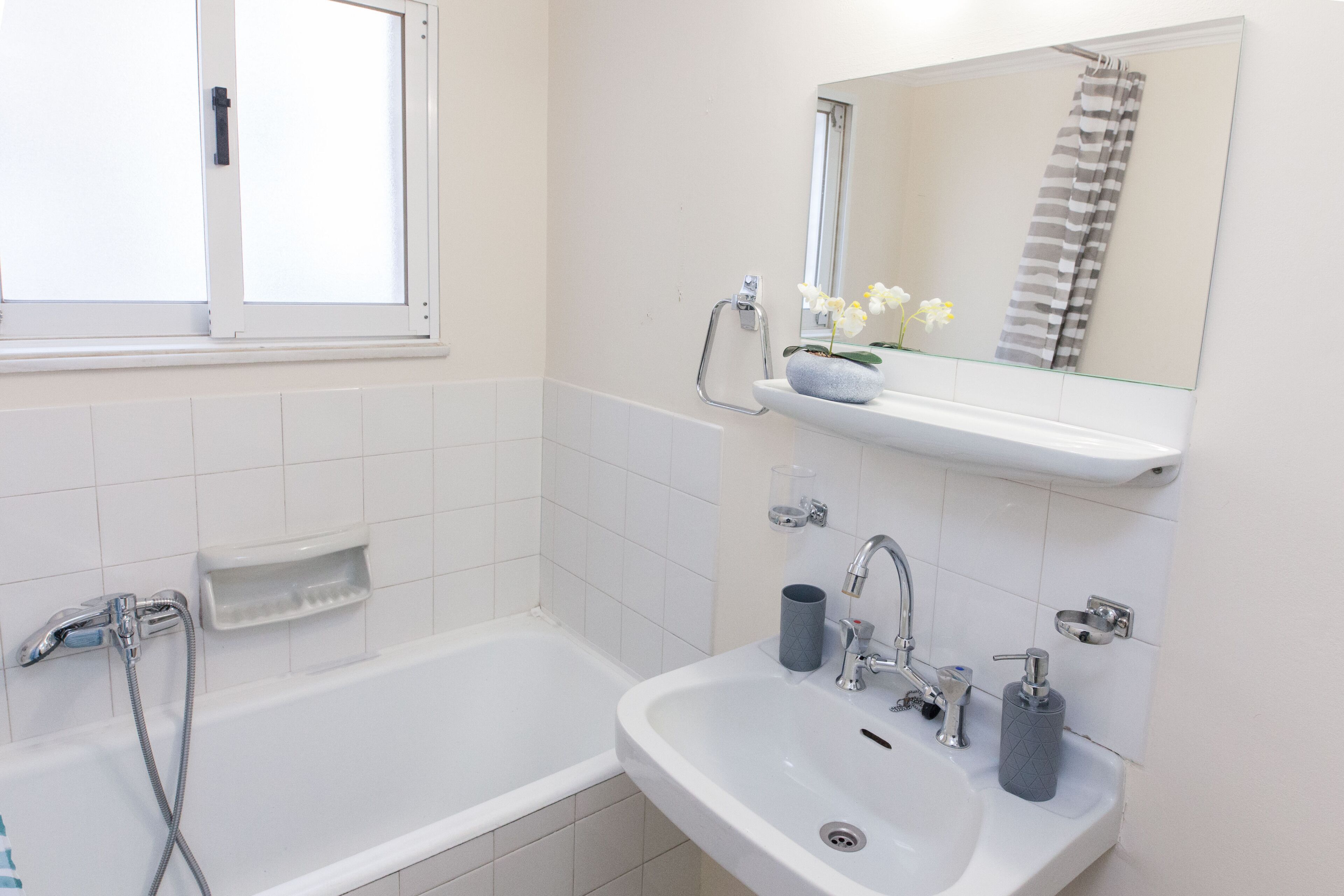 A bathroom with a bathtub, a sink, a mirror, and a window.