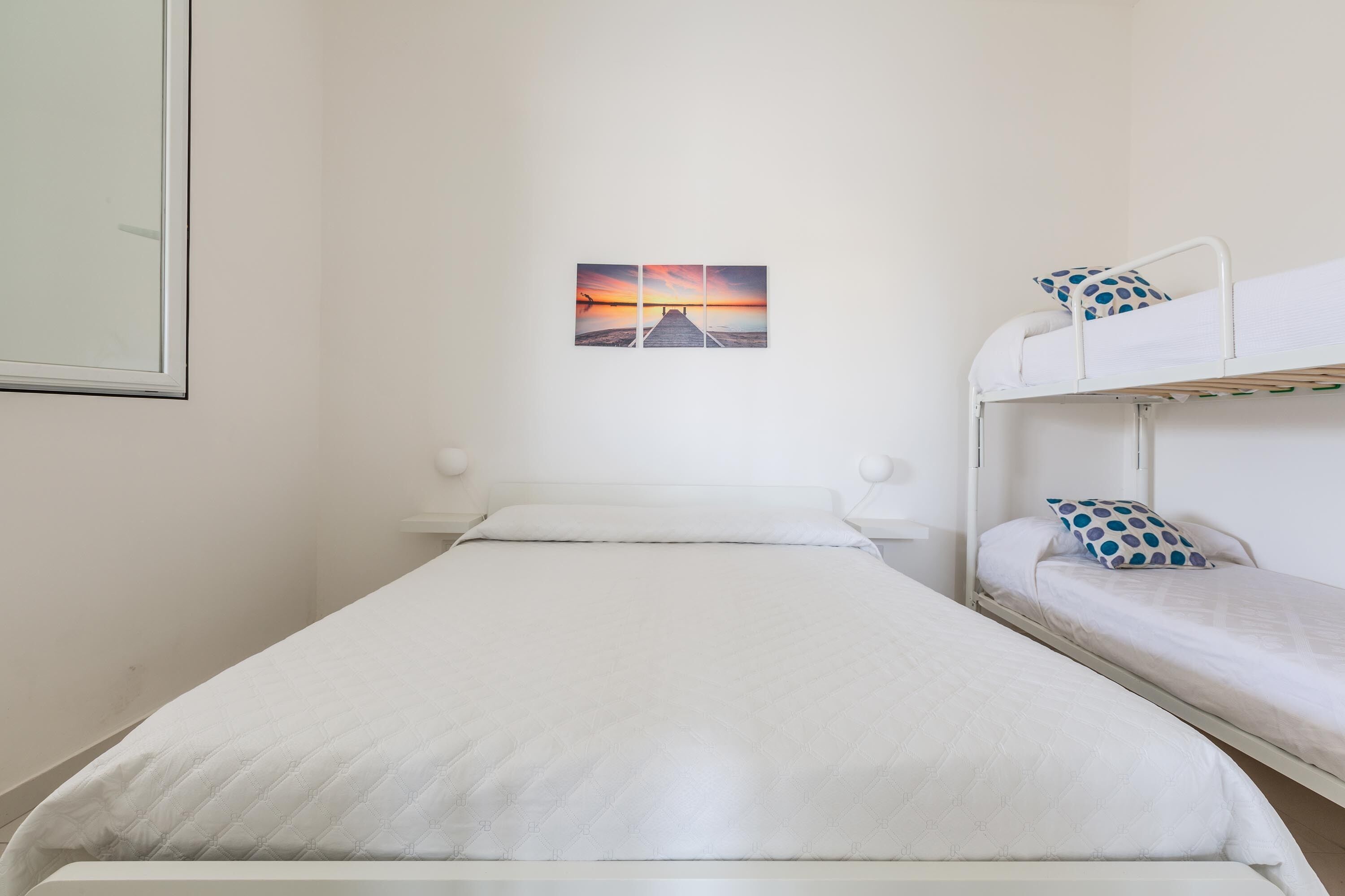A single bed with a white headboard and a bunk bed to the right. A framed picture hangs on the wall above the bunk bed.