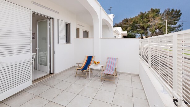 A balcony with two striped chairs and a small table, a sliding glass door, and a white railing. - 3700 La Spiaggetta - Bilo Lato by Barbarhouse (Porto Cesareo)