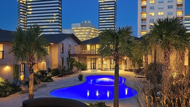 A modern hotel with a swimming pool, palm trees, and high-rise buildings in the background. - Dream House | 2BR Near Galleria (Houston)