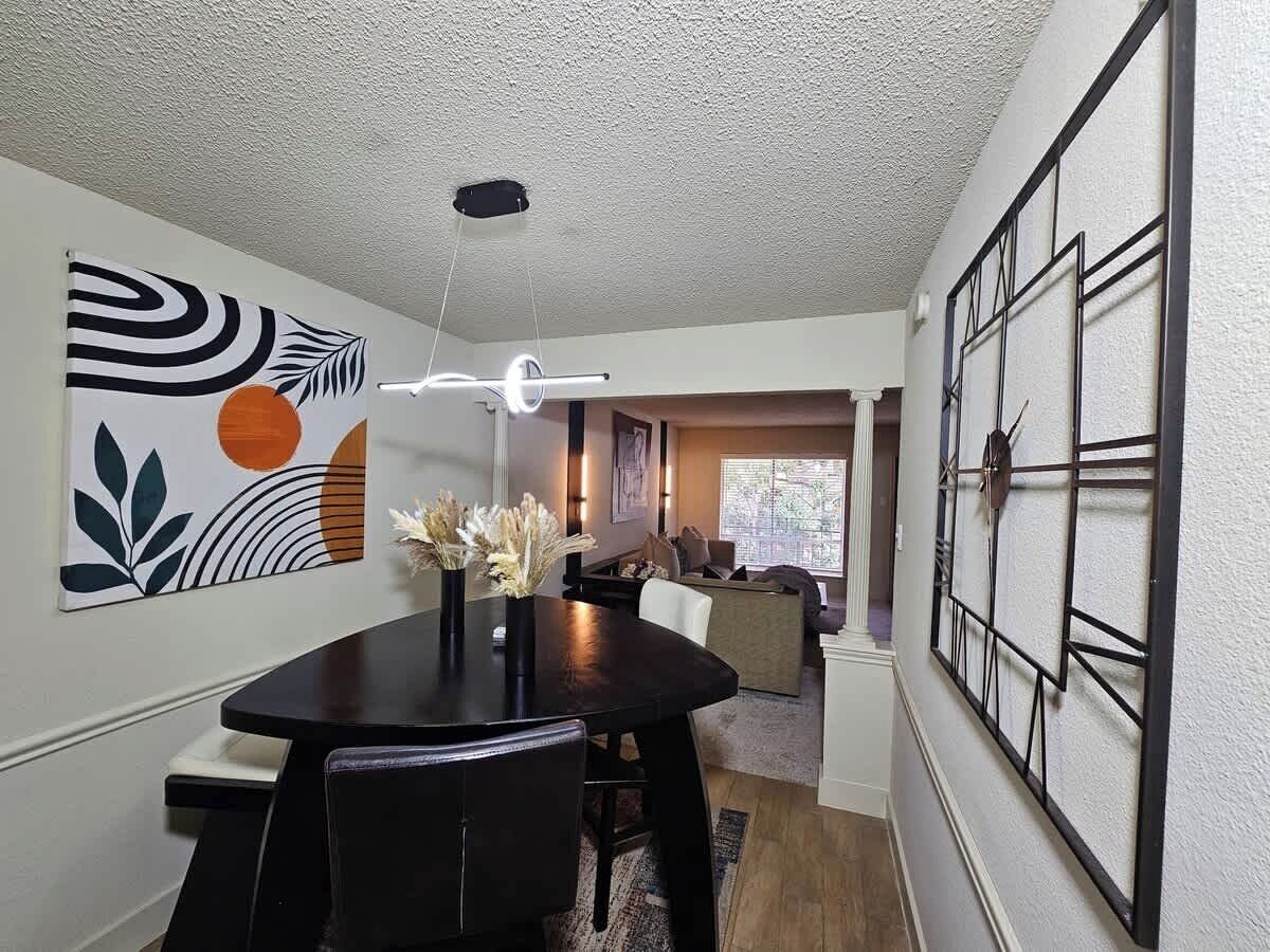 A dining area with a black table and chairs, a modern light fixture, and abstract wall art.