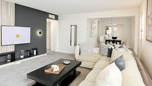 A modern living room with a black coffee table, a beige sofa, and a TV mounted on the wall. - Dream House | 2BR Near Galleria (Houston)