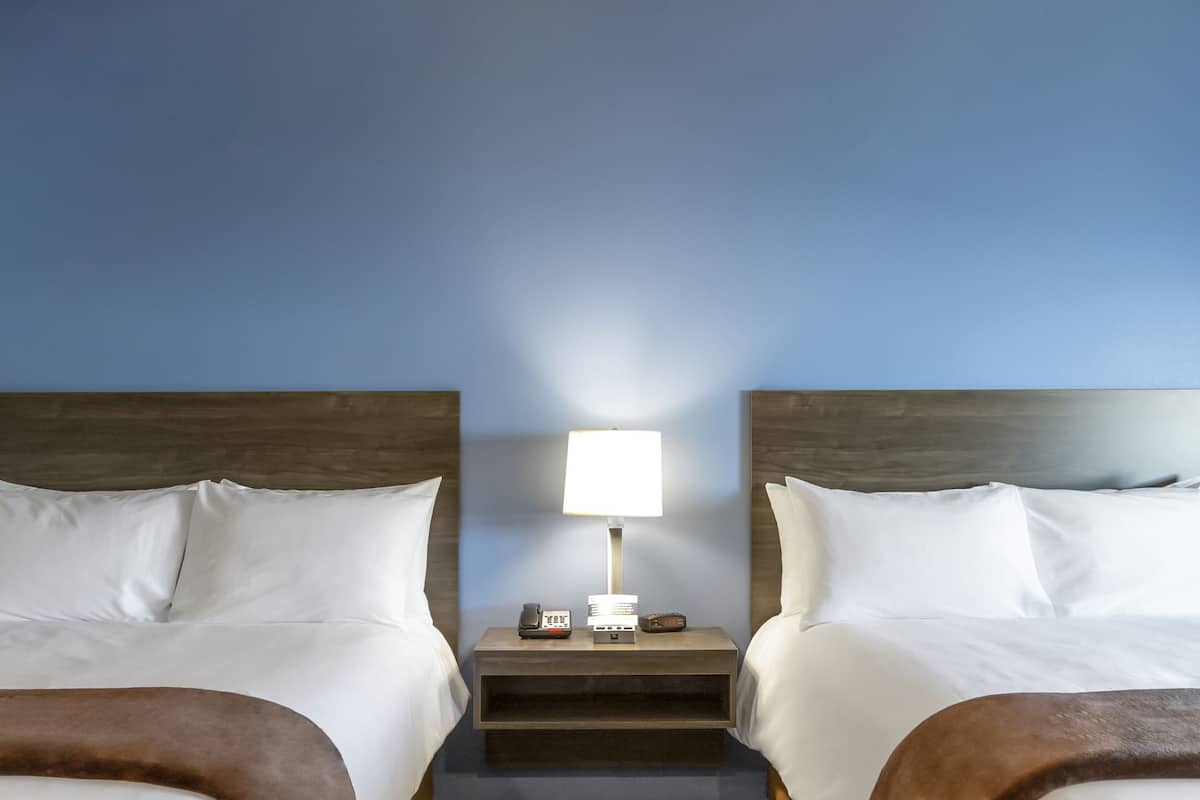 A hotel room with two beds, a nightstand with a lamp, and a phone.