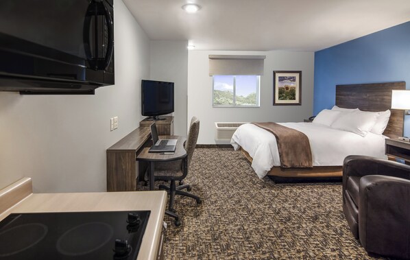 Habitación de hotel con cama, escritorio, silla, televisor y vistas al exterior.