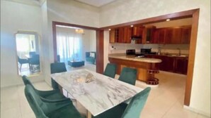 A modern kitchen with wooden cabinets and a dining area with a marble table and green chairs.