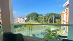 A view from a balcony overlooking a street with buildings, palm trees, and a clear sky.