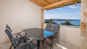 Un balcone con tavolo e sedie, affacciato su uno specchio d'acqua e un paesaggio lontano.