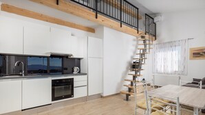 Una cucina moderna con mobili bianchi, un lavello in acciaio inossidabile e un forno integrato. Una scala a chiocciola conduce a una zona soppalco con pavimento in legno.