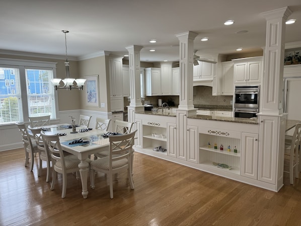 A spacious kitchen with white cabinetry, a dining area with a glass table, and a view of the city through large windows. - Stunning, Family sized, fully furnished home with pool at Spinnaker's Reach. (Emerald Isle)