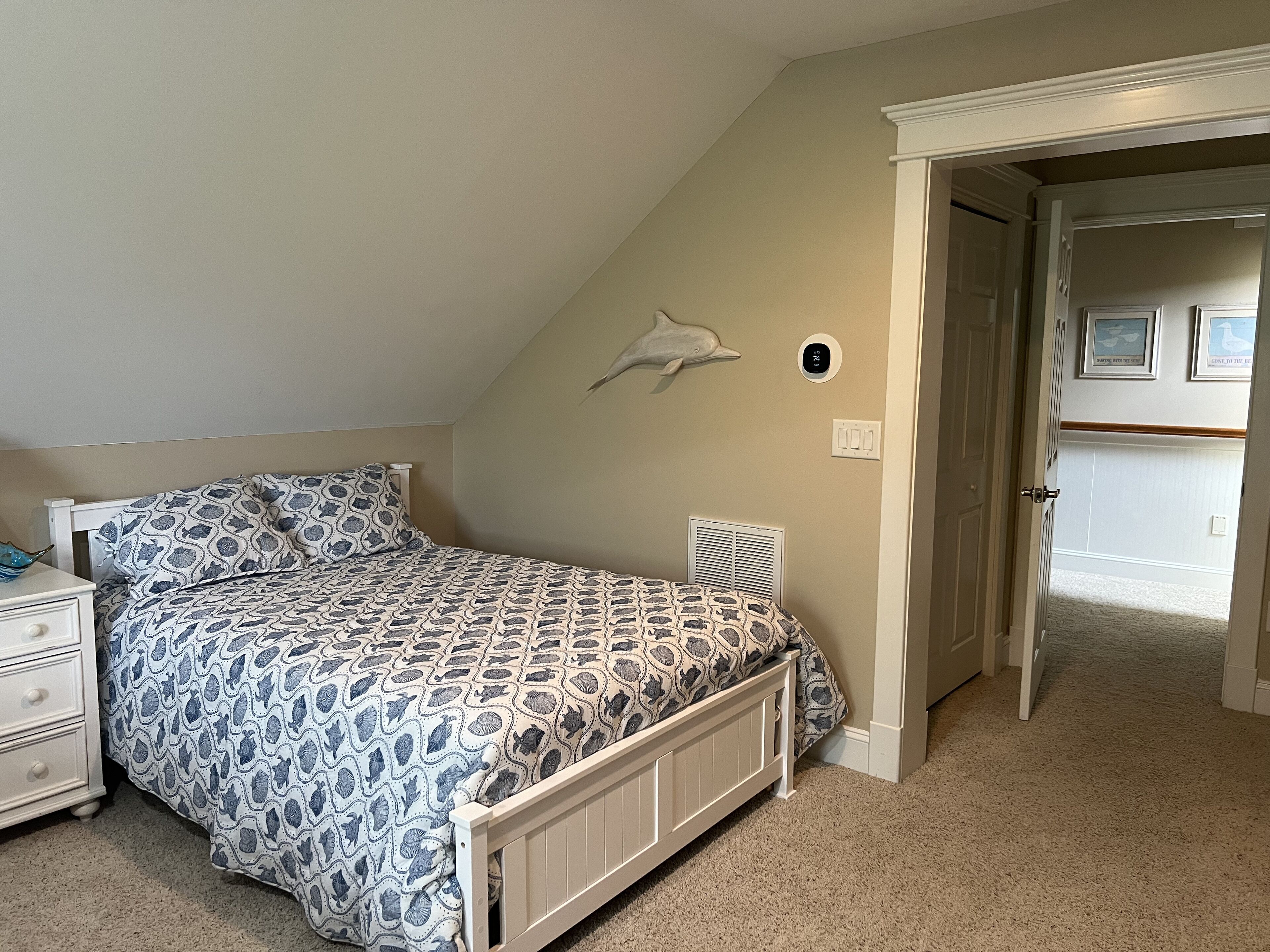 A bedroom with a bed, a nightstand, a wall-mounted heater, and a door leading to another room.