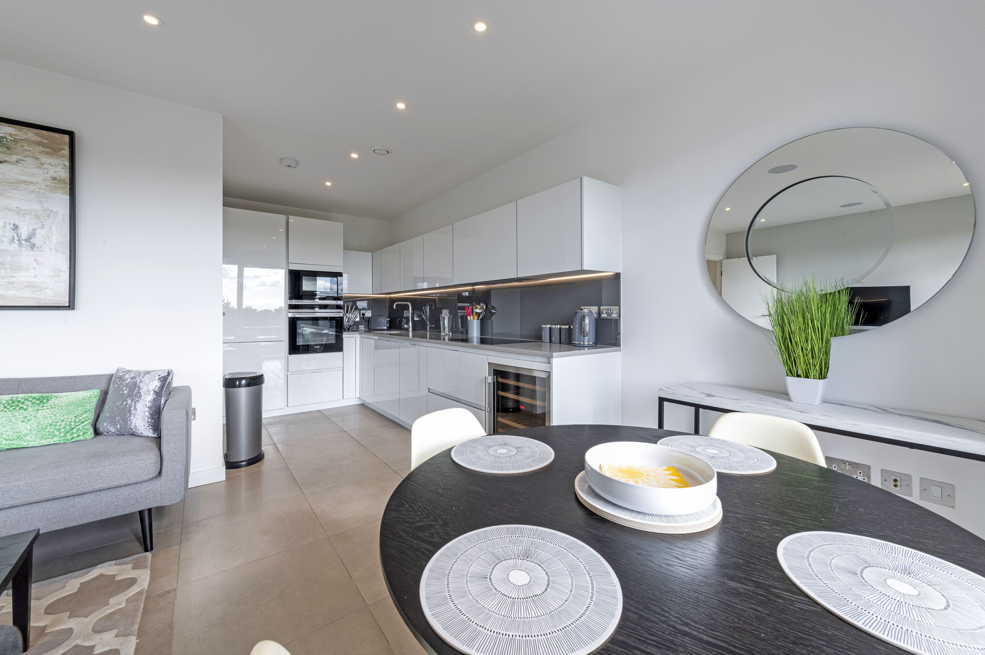 Une cuisine moderne avec des meubles blancs, une table à manger avec des sets de table et un grand miroir au mur.