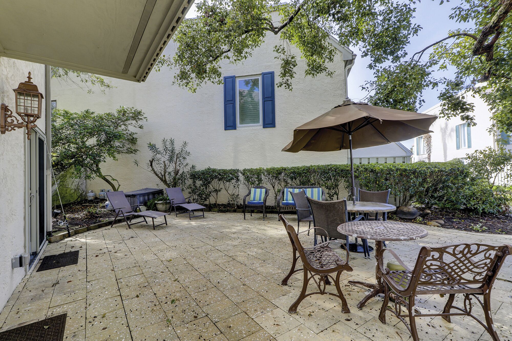 An outdoor patio with tiled flooring, wicker furniture, and a large umbrella providing shade.