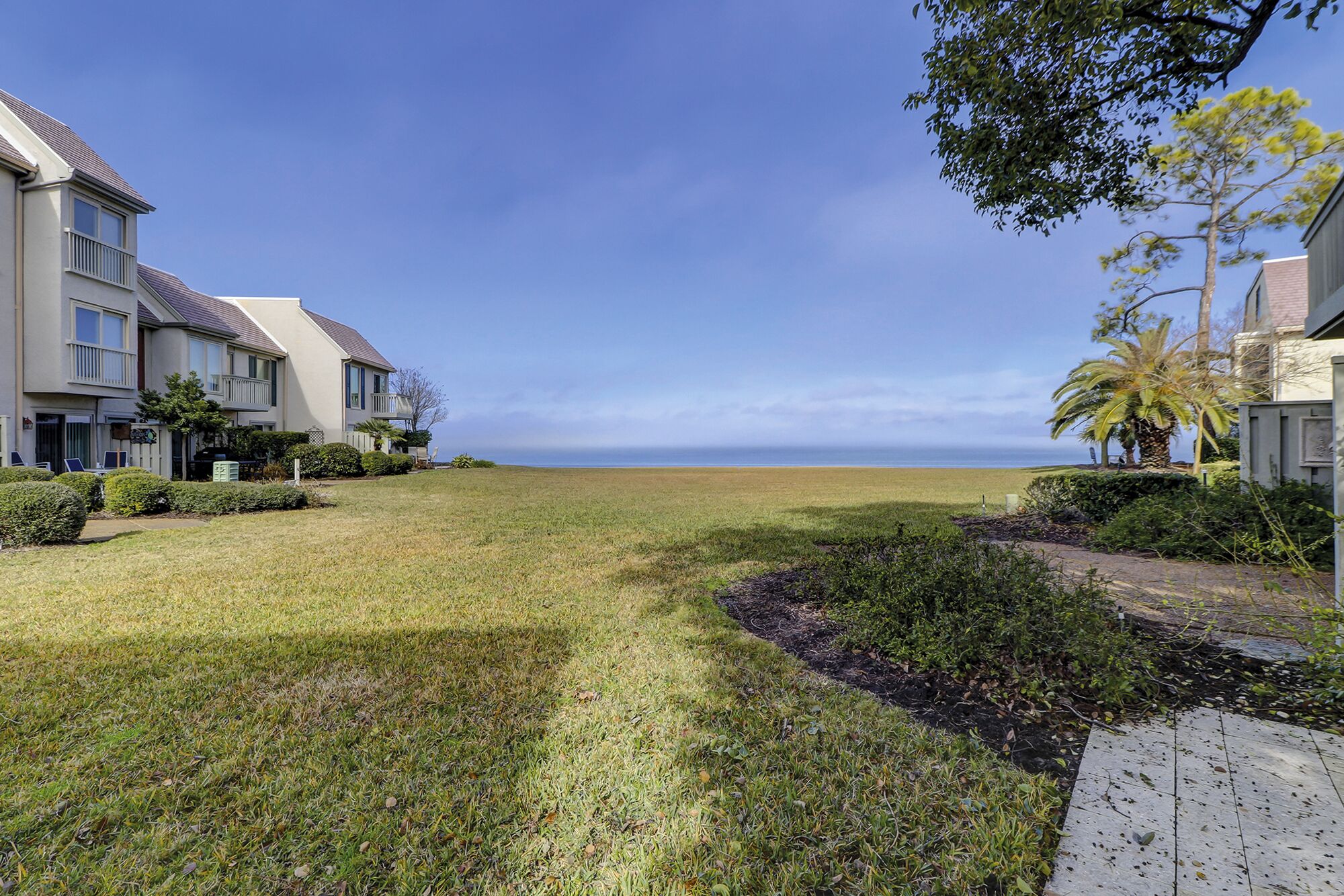 A residential area with a grassy pathway leading to a beach.