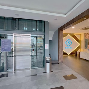 A hotel lobby with a reception desk, a glass elevator, and a trash bin. - S Hotel (Johor Bahru)