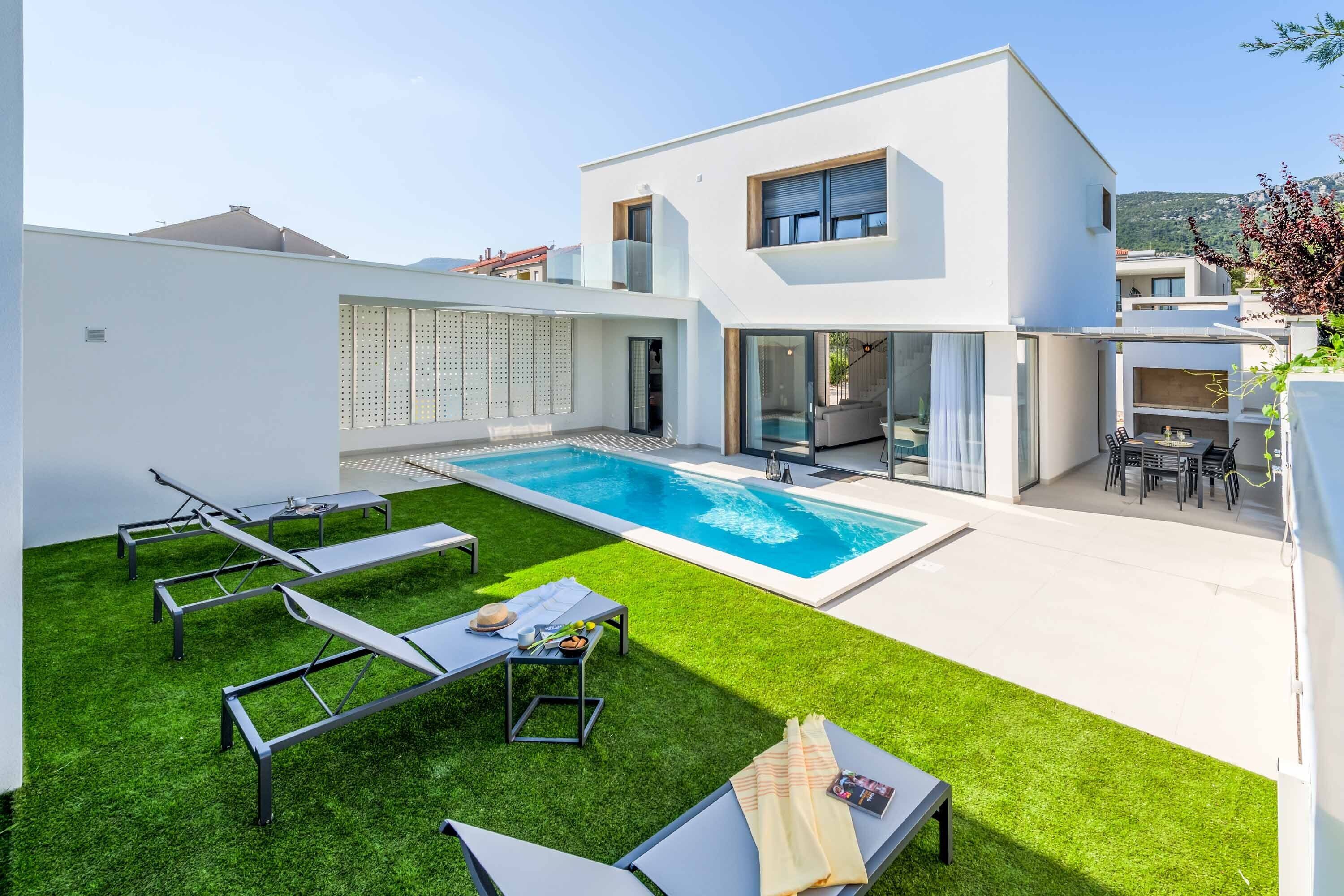 Ein modernes Haus mit Swimmingpool, einer Terrasse mit Liegestühlen und einem gepflegten Rasen.