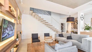 A modern living room with a staircase, a flat-screen TV, and a bookshelf.