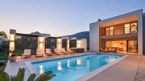 A modern poolside area with lounge chairs and a hot tub, surrounded by a white building with large windows.