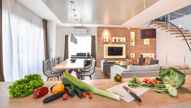 A modern kitchen with a dining area, a staircase, and a living room with a sofa and TV.