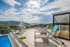 Une terrasse sur le toit dotée d’une piscine, de chaises longues et d’un fauteuil suspendu, offrant une vue imprenable sur un paysage magnifique.