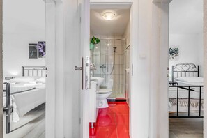 Un baño moderno con cabina de ducha de vidrio, sanitarios blancos y suelo de baldosas rojas.