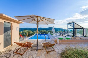 Un área de piscina con un columpio, sillones de descanso y una estructura de cristal.
