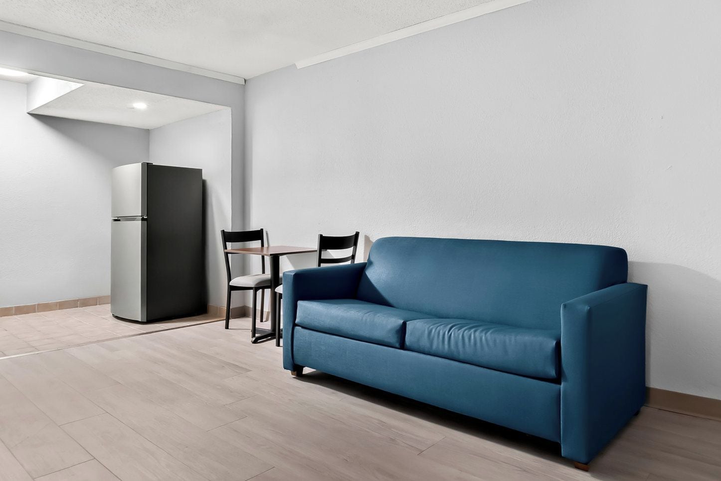 A modern living room with a blue sofa, a small table, two chairs, and a refrigerator.