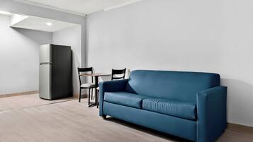 A modern living room with a blue sofa, a small table, two chairs, and a refrigerator.